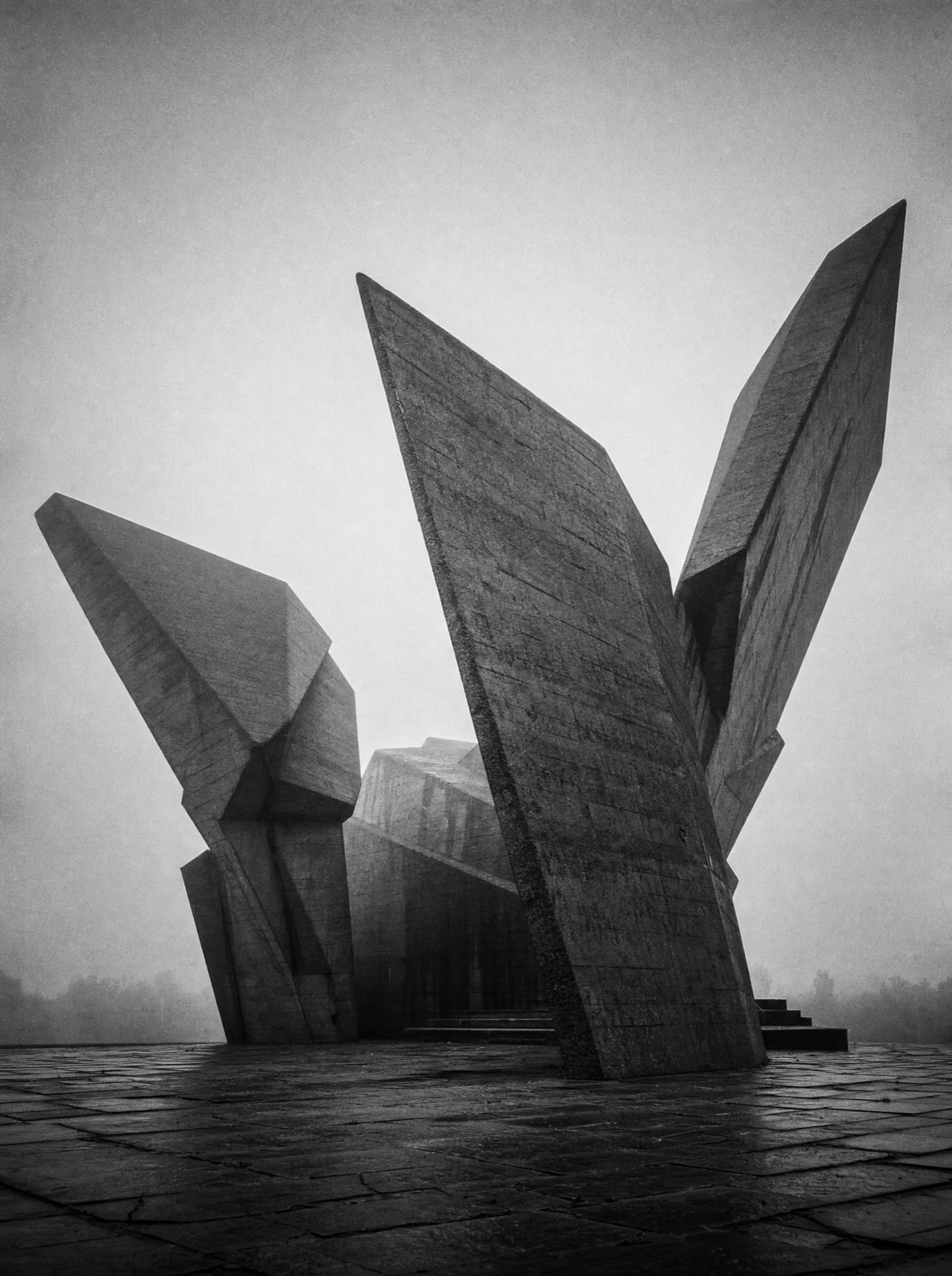 Two winged concrete blades of a memorial monument rising out of plateau fog