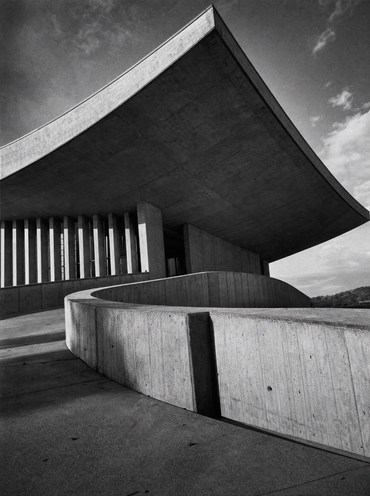 Sweeping curved concrete canopy over a thin colonnade and curving rampart wall